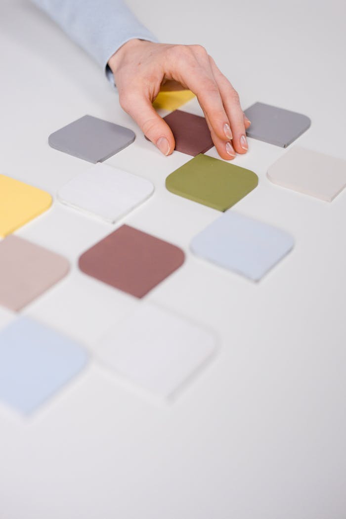 Close-up of a hand arranging diverse color swatches on a white table.